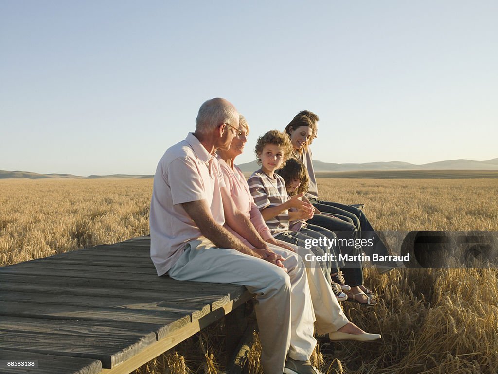 Family sitting on wooden dock in remote wheat field