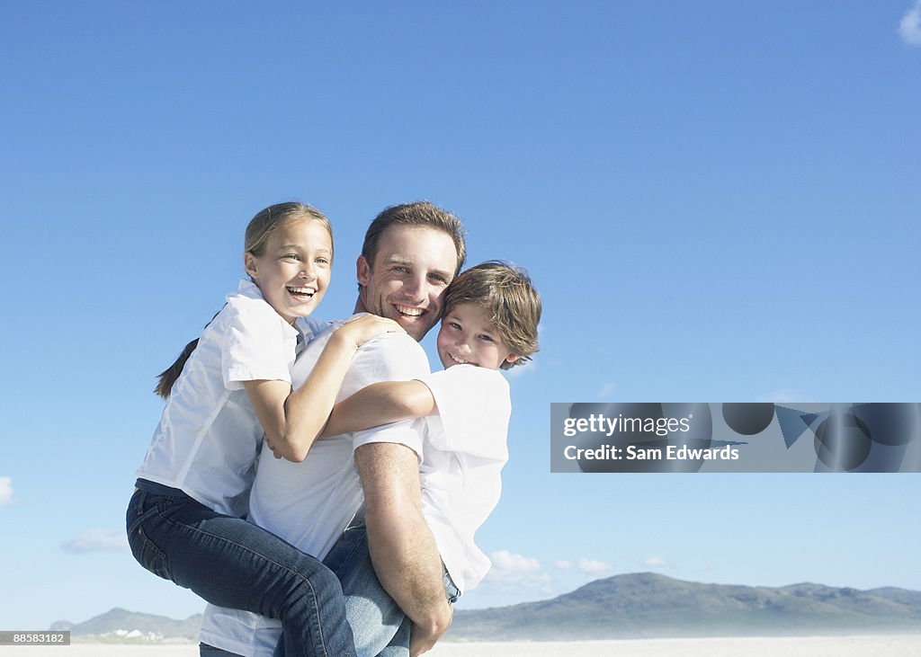 Father carrying children at beach