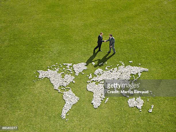 businessmen shaking hands near world map made of rocks - global fashion collective stock pictures, royalty-free photos & images