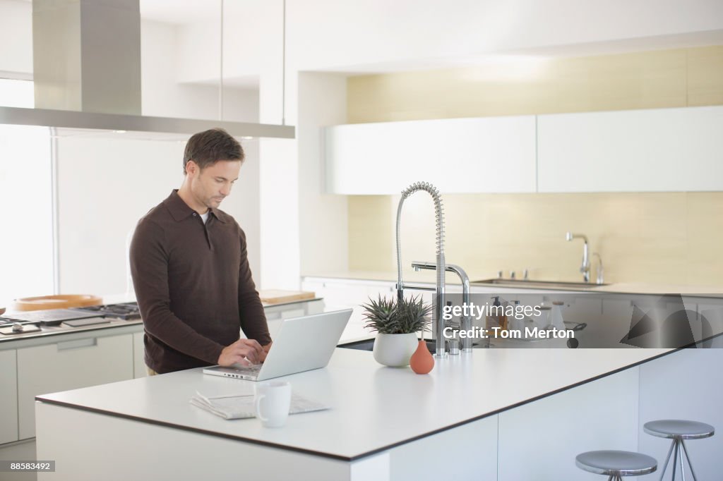 Homme utilisant un ordinateur portable dans la cuisine