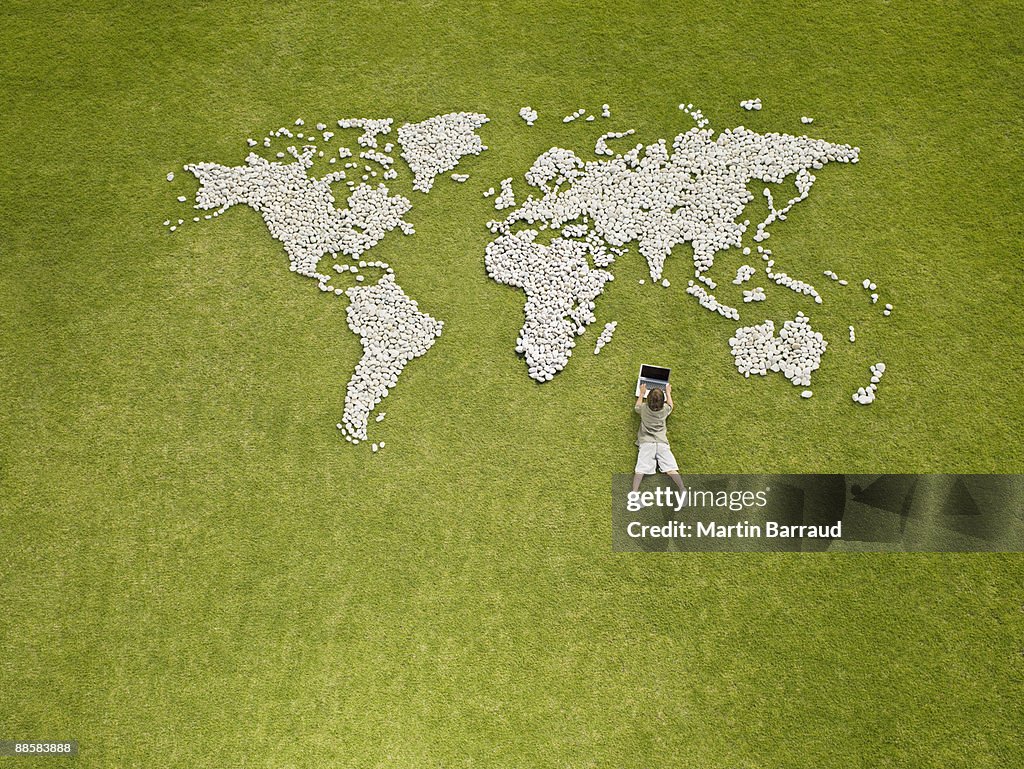 Boy using laptop near world map made of rocks