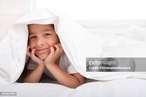 布団の下で笑顔の小さな男の子 - six under ストックフォトと画像