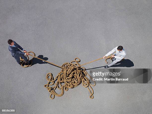 businessmen pulling at tangled rope - untangle stock-fotos und bilder