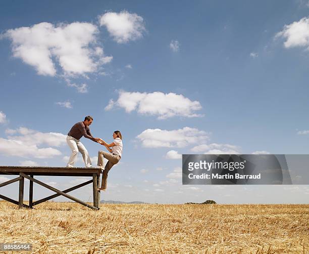 man helping woman up wooden dock in field - pull foto e immagini stock
