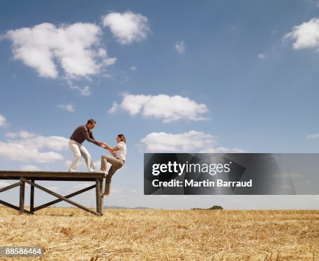 Man helping woman up wooden dock in field