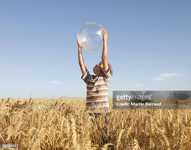 boy holding clear globe in field - holding globe stock pictures, royalty-free photos & images