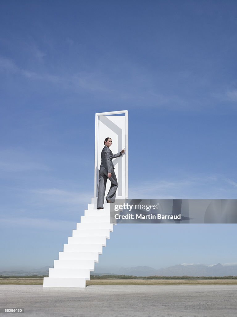 Businesswoman opening door at end of stairway leading to the sky