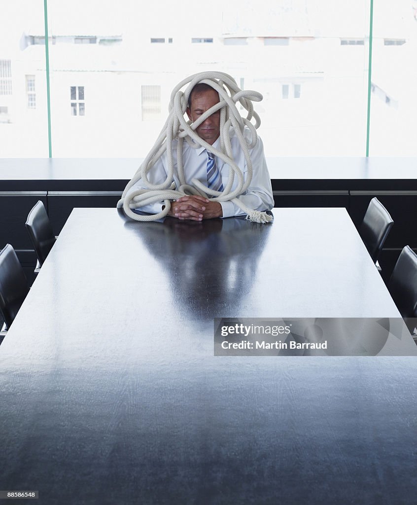 Businessman tangled in rope in conference room