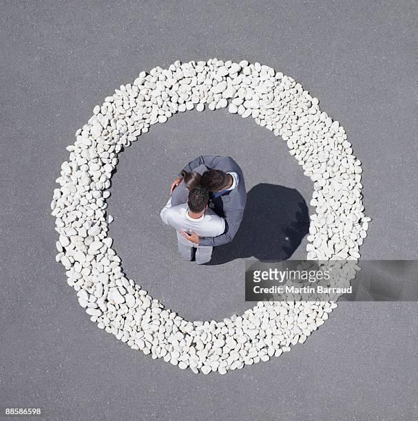 businesspeople huddling inside rock circle - circondare foto e immagini stock