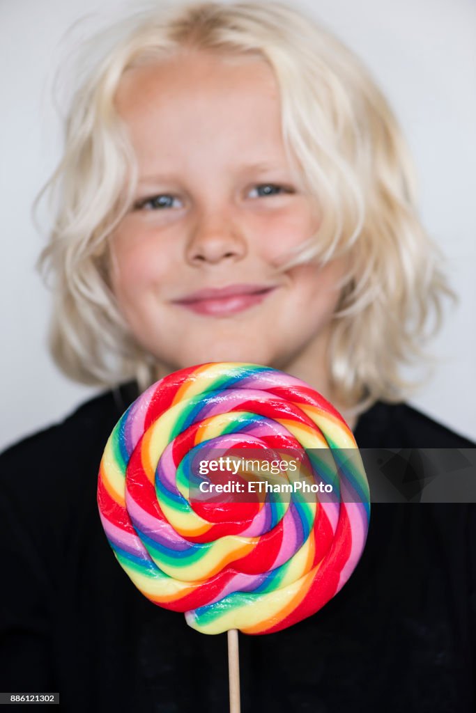 10 year-old blond boy eating large colorful lollipop