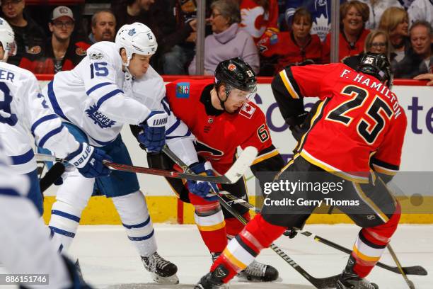 Matt Martin of the Toronto Maple Leafs, Brett Kulak and Freddie Hamilton of the Calgary Flames battle for the puck in an NHL game against the Toronto...