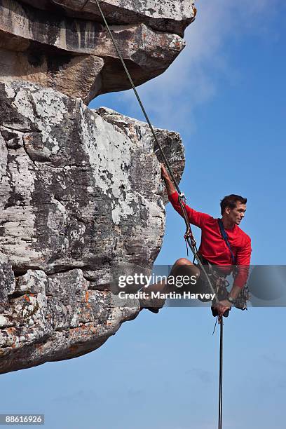 male rock climber abseiling down cliff face. - abseiling stock pictures, royalty-free photos & images