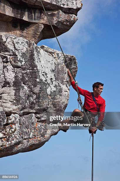 male rock climber abseiling down cliff face. - rappelling stock pictures, royalty-free photos & images