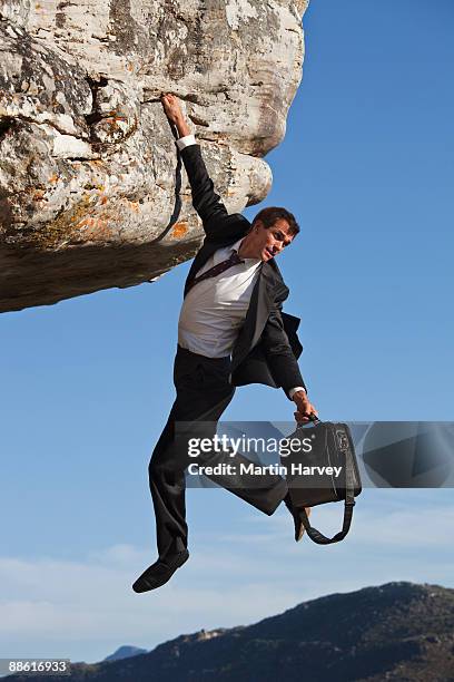 businessman with briefcase clinging onto cliff - suits hanging stock pictures, royalty-free photos & images