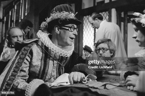 British film and television charactor actor Richard Wattis, dressed in Elizabethan costume, photographed with actors and crew on a film set on 16th...