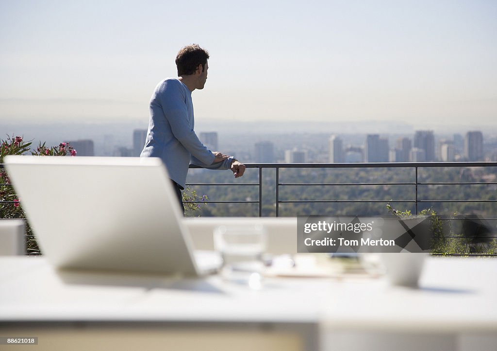 Mann mit laptop auf Balkon mit Blick auf die Stadt