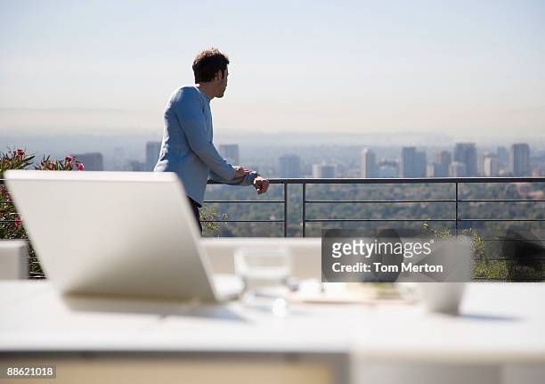 hombre usando una computadora portátil en el balcón con vista a la ciudad - barandilla fotografías e imágenes de stock