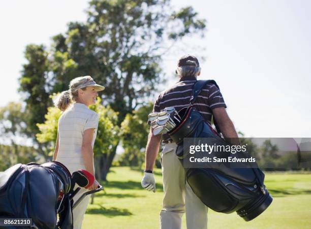 mature couple carrying golf bags - golf bag stock pictures, royalty-free photos & images