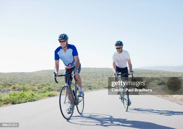 men riding bicycles on remote road - man cycling stock pictures, royalty-free photos & images