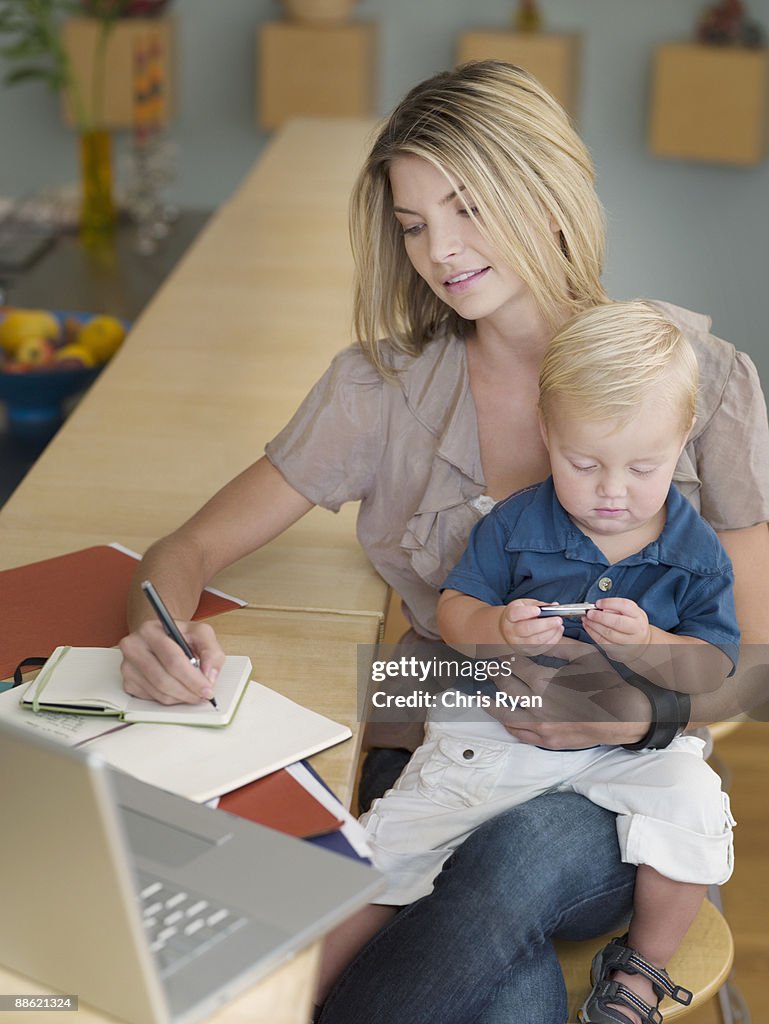 Mother working and holding son on lap