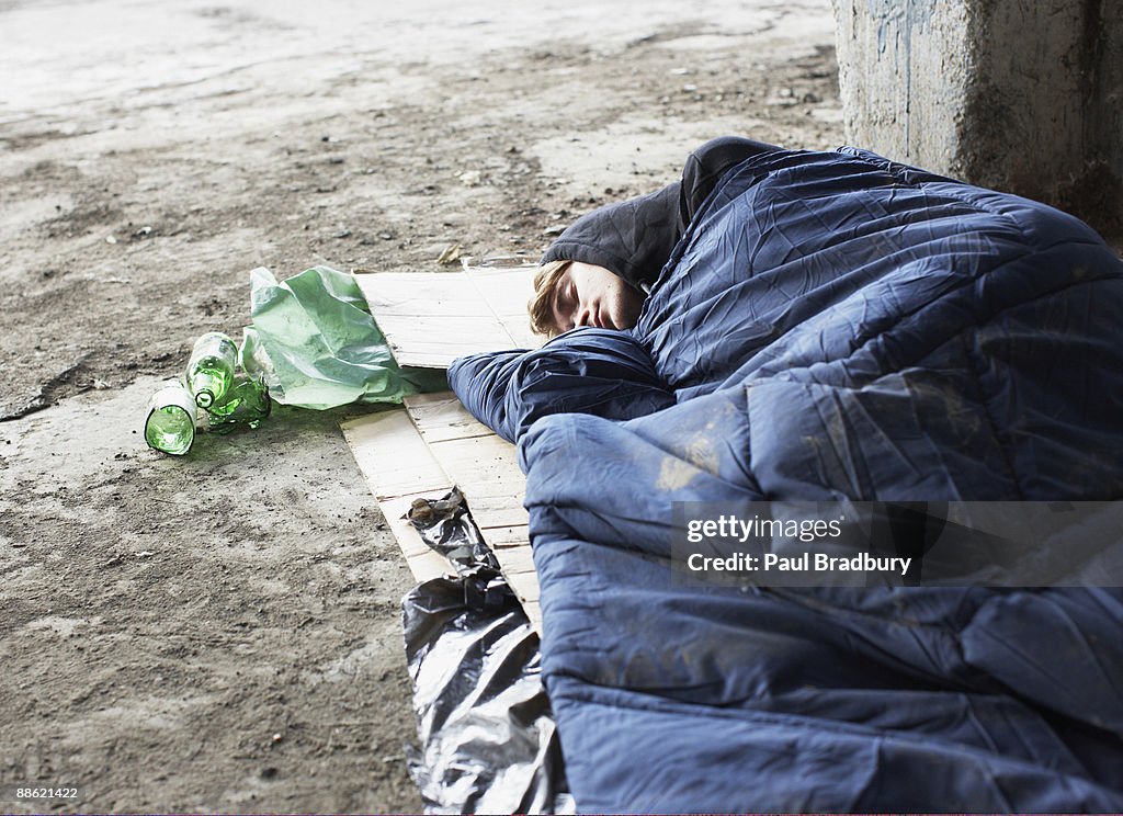 Homeless man sleeping in sleeping bag on cardboard