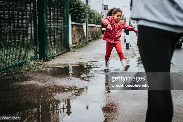 siblings jumping over puddles - onebluelight stock pictures, royalty-free photos & images