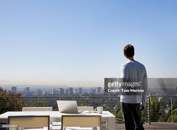 man using laptop on balcony overlooking city - three quarter length stock pictures, royalty-free photos & images