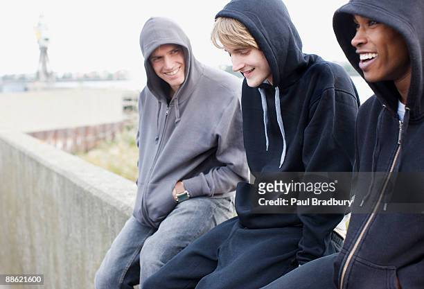 drei junge männer in kapuzenjacken sitzt an der wand - london young people black and white stock-fotos und bilder