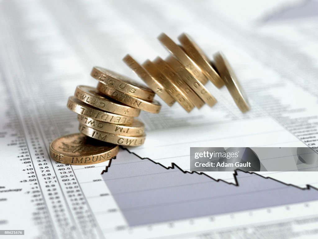 Stack of British pound coins falling on list of share prices