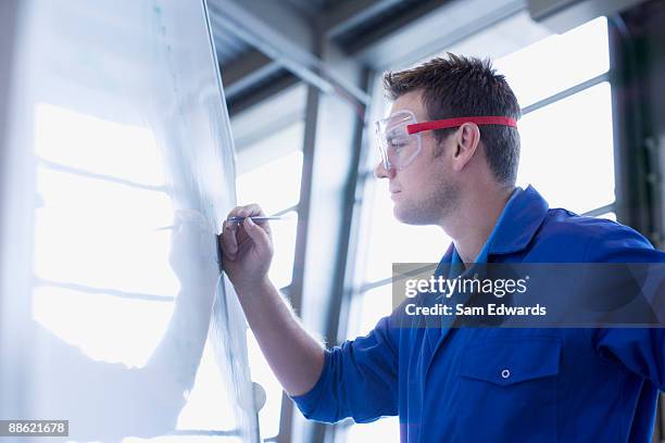 man in coveralls writing on whiteboard - eye-protection stock pictures, royalty-free photos & images