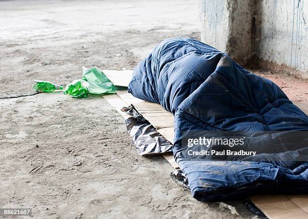 homeless man sleeping in sleeping bag on cardboard - homelessness stockfoto's en -beelden