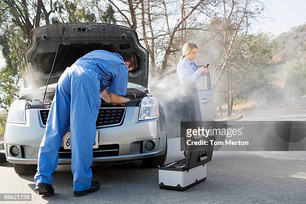 businesswoman using cell phone while mechanic looks at car engine - vehicle hood stock pictures, royalty-free photos & images