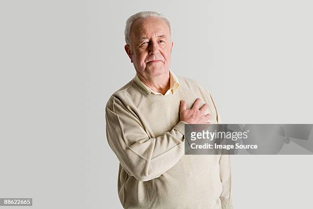 senior man with hand on heart - borstkas stockfoto's en -beelden
