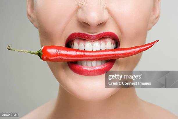 woman with a red chili pepper between her teeth - red pepper stock pictures, royalty-free photos & images