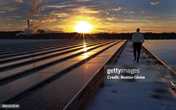 Costa Nicolaou, whose PanelClaw company makes mountings for solar panels, walks among rows of solar panels on the roof of a building at Osgood...