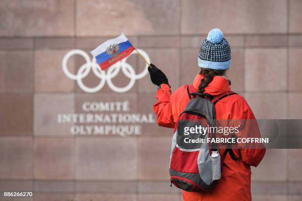 Supporter waves a Russian flag in front of the logo of the International Olympic Committee at their headquarters on December 5, 2017 in Pully near...