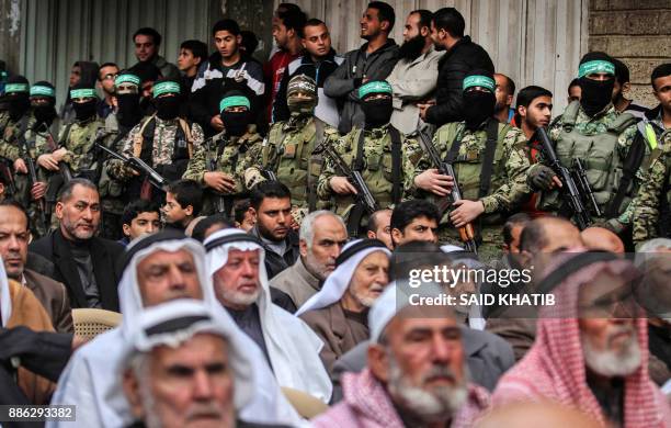 Palestinian men watch as fighters from the Ezzedine al-Qassam Brigades, the armed wing of the Palestinian Hamas movement, take part in a military...