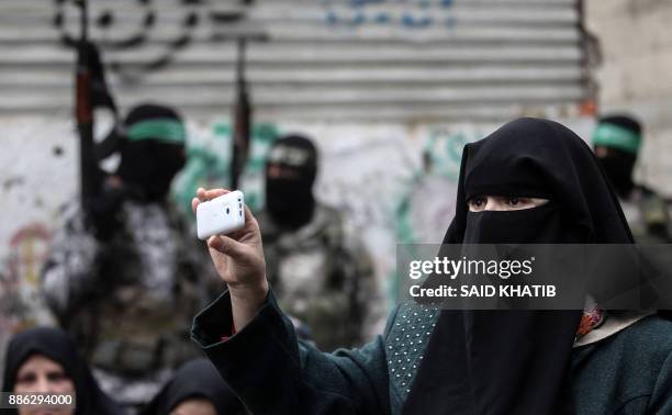 Palestinian woman uses her cell phone to film as fighters from the Ezzedine al-Qassam Brigades, the armed wing of the Palestinian Hamas movement,...