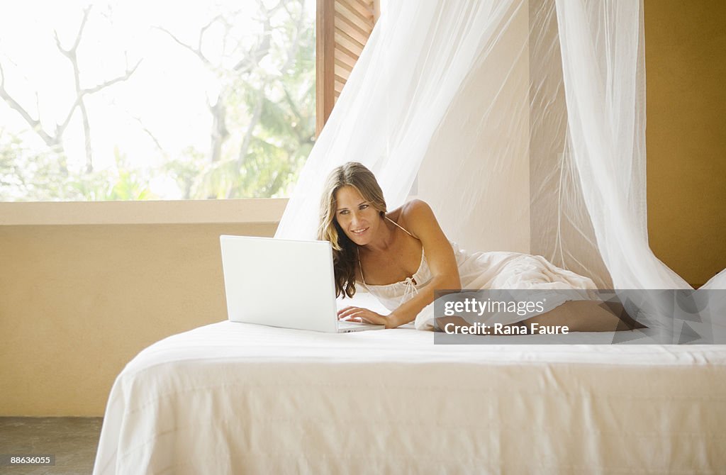 Young woman on a bed tropical with laptop