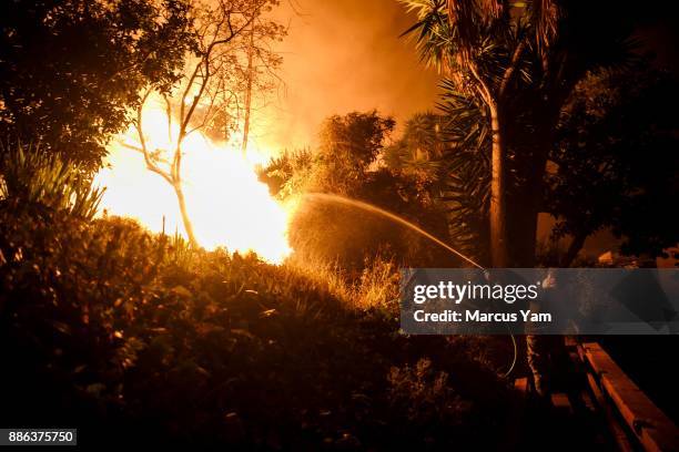 Al Galileo helps water down a backyard of a stranger's home as brush fire encroaches on the property on December 5, 2017 in Ventura, California.