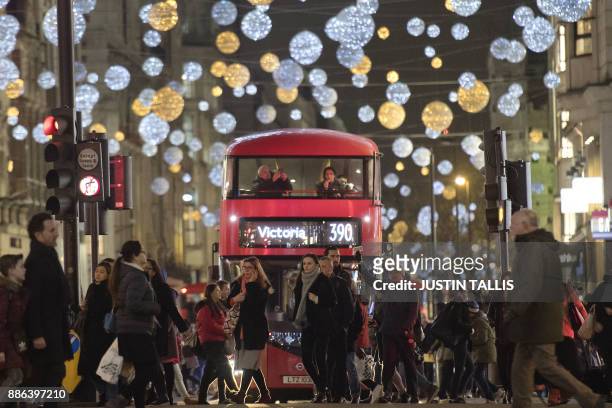 Shoppers cross in front of a London bus as it travels under Christmas lights on Oxford Street, in central London on December 5, 2017. / AFP PHOTO /...