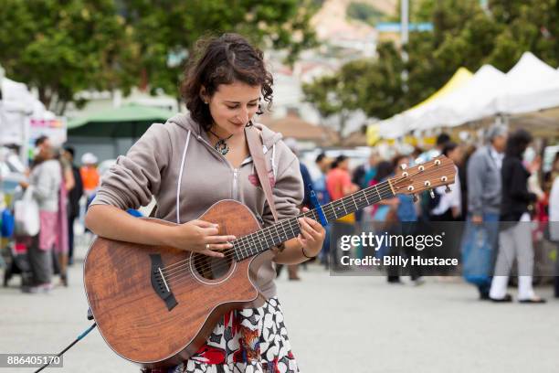a smiling young woman in casual dress playing a guitar at a farmer's market. - musica acustica fotografías e imágenes de stock