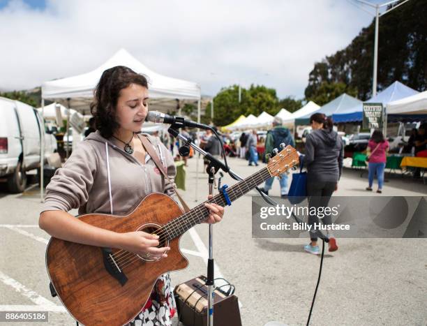 a young musician singing into a microphone while playing a guitar at an organic farmer's market. - street artist stock pictures, royalty-free photos & images