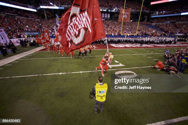 Big 10 Championship: Ohio State cheerleader with mascot Brutus Buckeye taking field, carrying OHIO STATE flag before game vs Wisconsin at Lucas Oil...