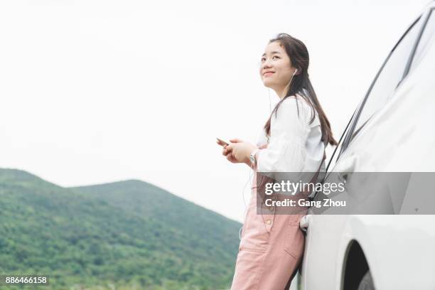 asian woman leaning against car listening to music - leaning on car pose stock pictures, royalty-free photos & images