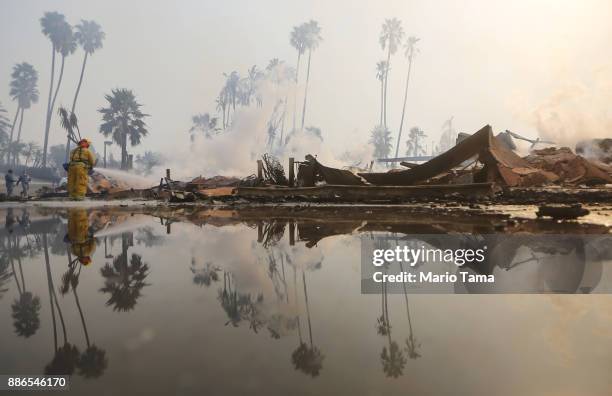 Firefighter sprays water at the remains of an apartment complex destroyed by the Thomas Fire on December 5, 2017 in Ventura, California. Around...