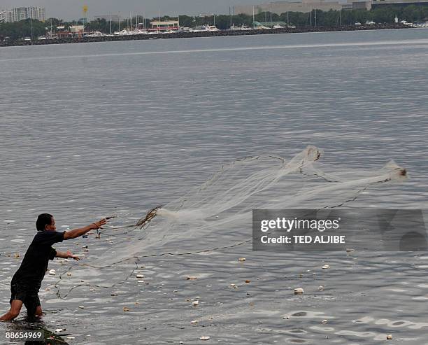 Man throws a fishing net into the sea along Manila Bay on June 24, 2009 as weather forecasters warn of typhoon Nangka hitting Manila around 10 pm...