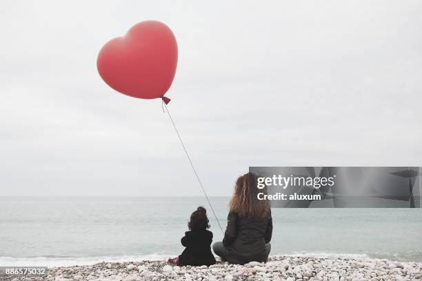 woman with baby girl and heart balloon looking at the sea - heart vs mind stock pictures, royalty-free photos & images