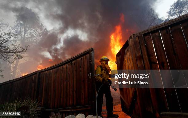 Firefighter wets down a fence to protect a house across the street from a residence that is engulfed in flames near the intersection of Johanna...