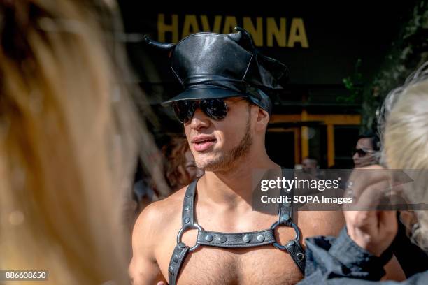 Man dressed in a leather hat and costume marches for LGBTQIA+ pride with a Havana coffee house in the background. Thousands of pride supporters...